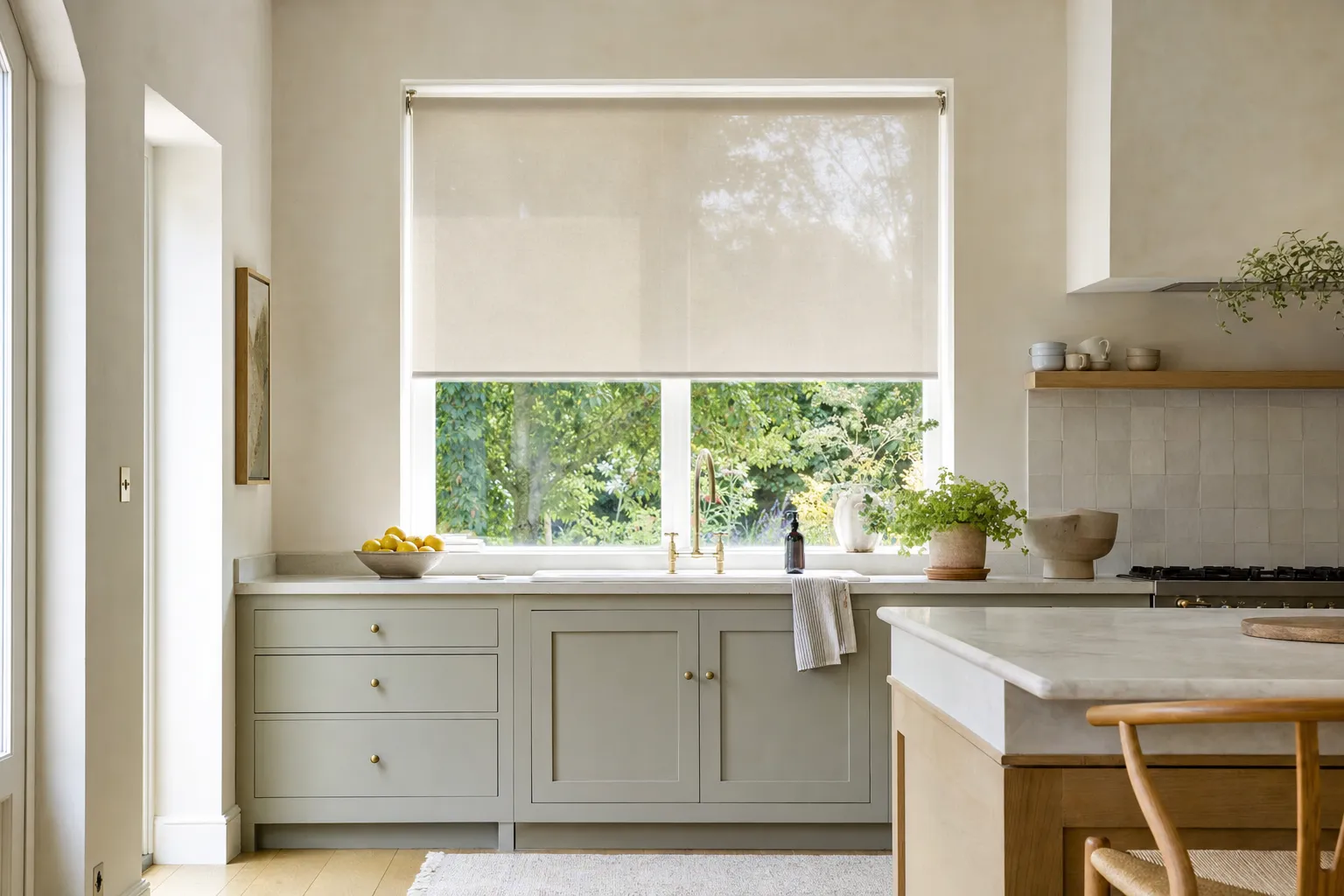 A roller blind lowered halfway over a bright kitchen window, one flat continuous plane of screen fabric with the garden visible below it