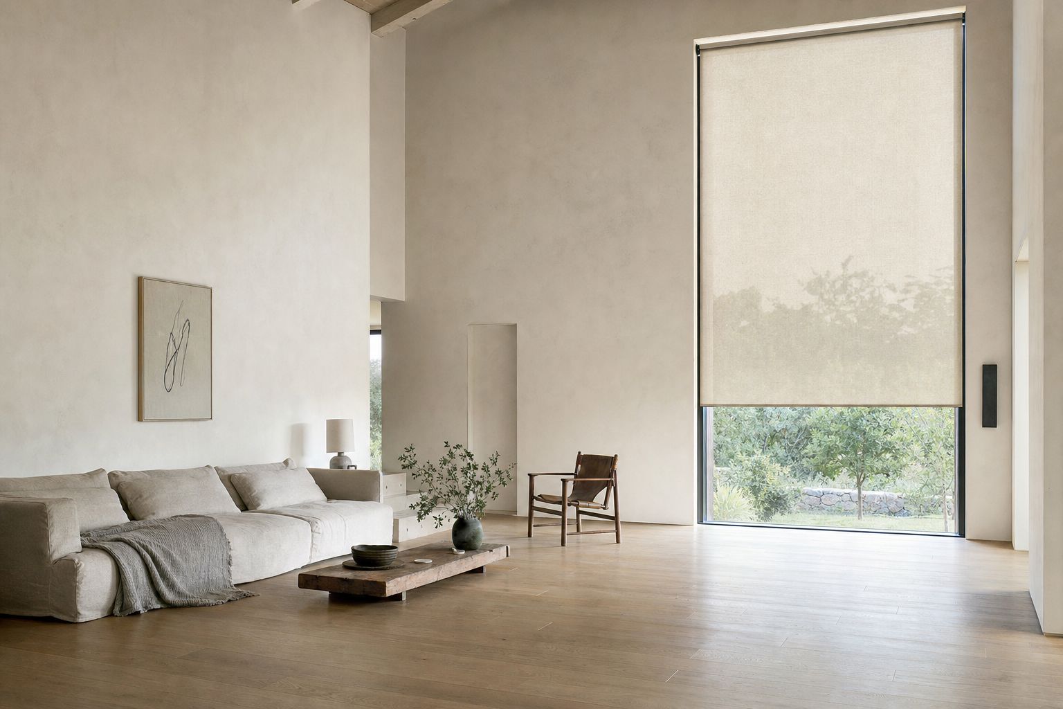 A wide, bright room with a tall window on the right carrying a single roller blind — one flat continuous plane of screen fabric with the garden faintly visible through the weave, and clear glass below it